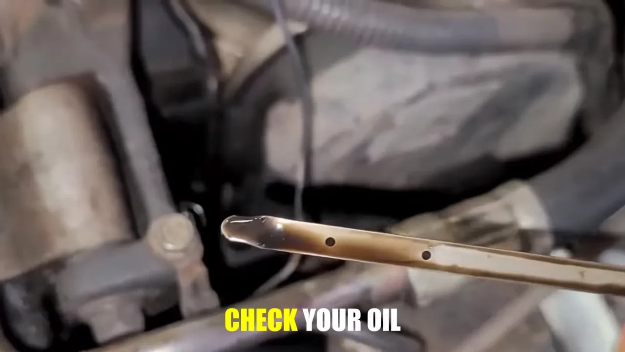 Close-up of an oil-coated dipstick held above engine components