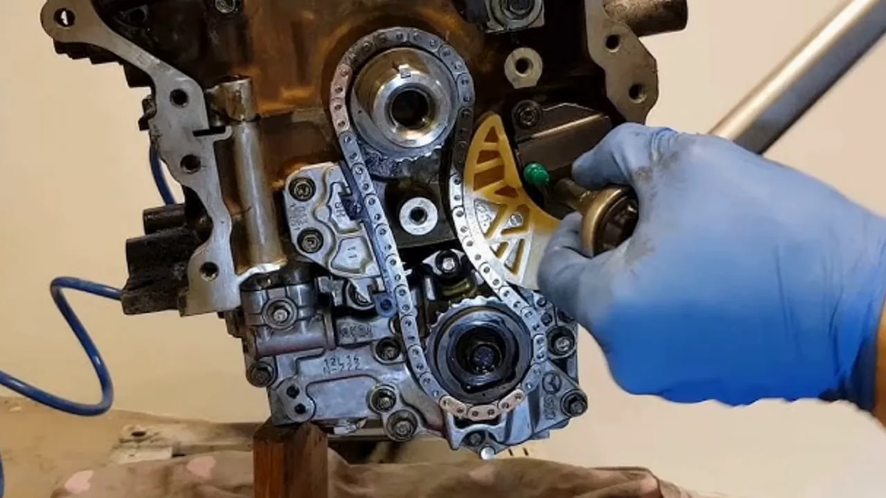 Exposed chain and sprockets beside a blue-gloved hand