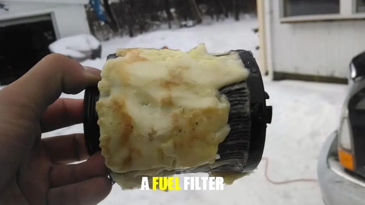 Hand holding a pleated filter element covered in pale deposits outdoors in snowy conditions