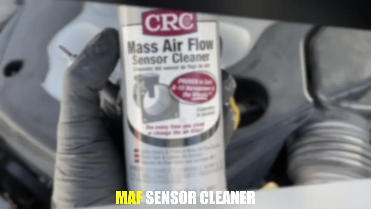 Gloved hand holding a can labeled Mass Air Flow Sensor Cleaner beside an engine