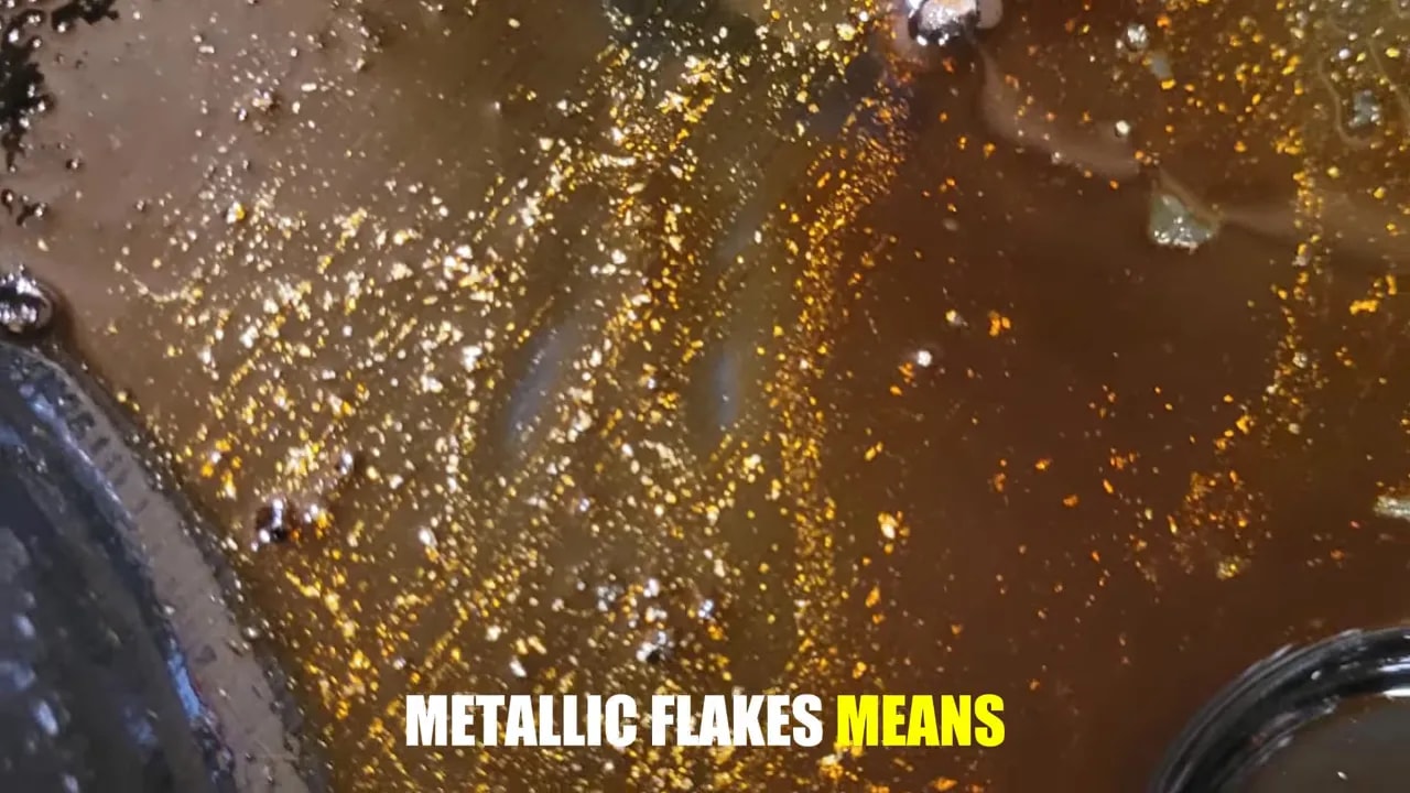 Close-up of dark oil containing numerous bright metallic-looking particles