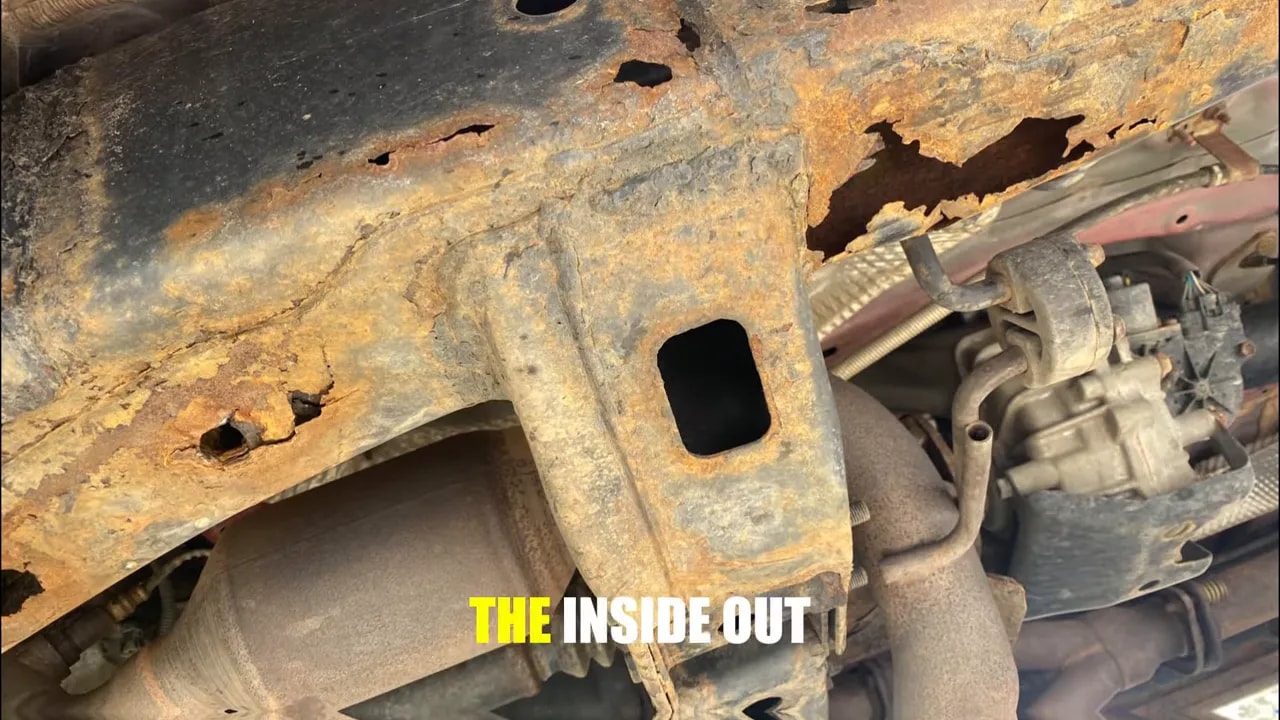 Heavily corroded truck frame with jagged holes and flaking metal