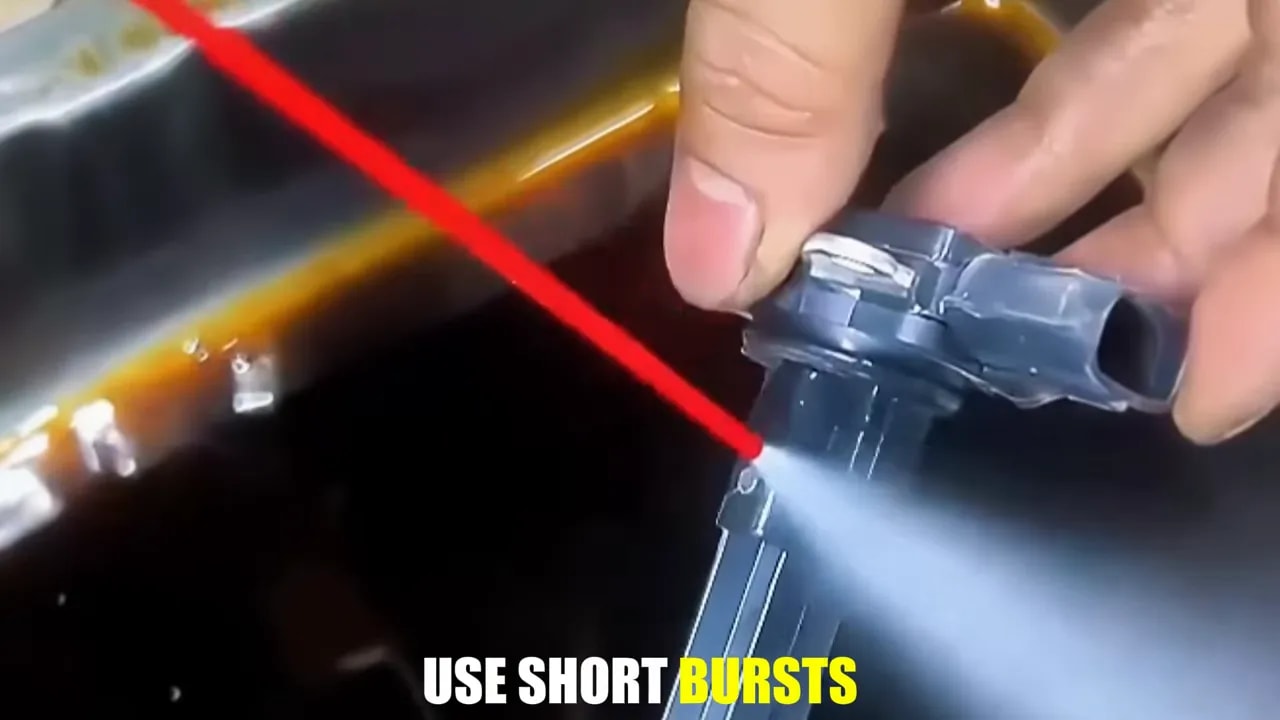 Hands holding a removed MAF sensor while a red spray straw directs cleaner toward its sensing area